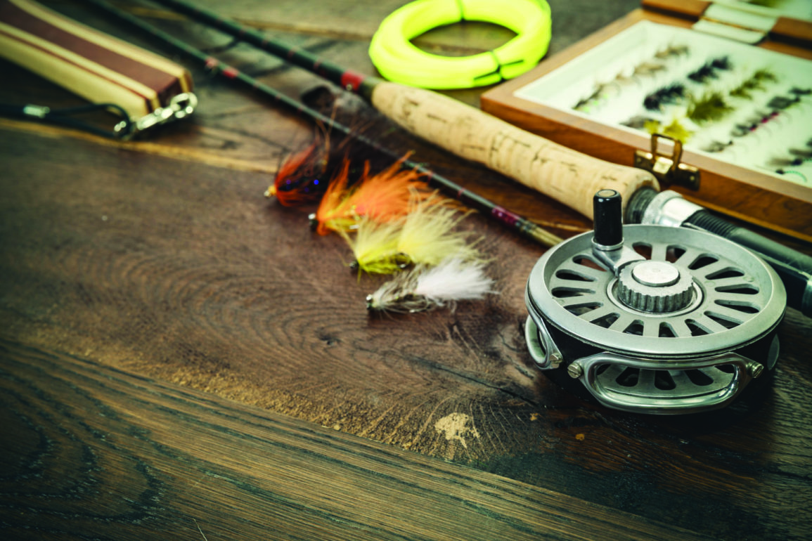 Net, fishing rod, set by river for fly fishing on an old wooden table. Photo by iStock.