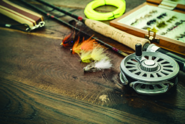 Net, fishing rod, set by river for fly fishing on an old wooden table. Photo by iStock.