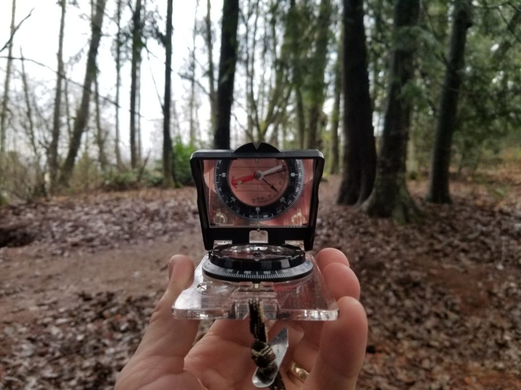 Using a sighting compass, as shown, is the most accurate way to navigate along your chosen direction. Note how the face of the compass is visible in the sighting mirror.