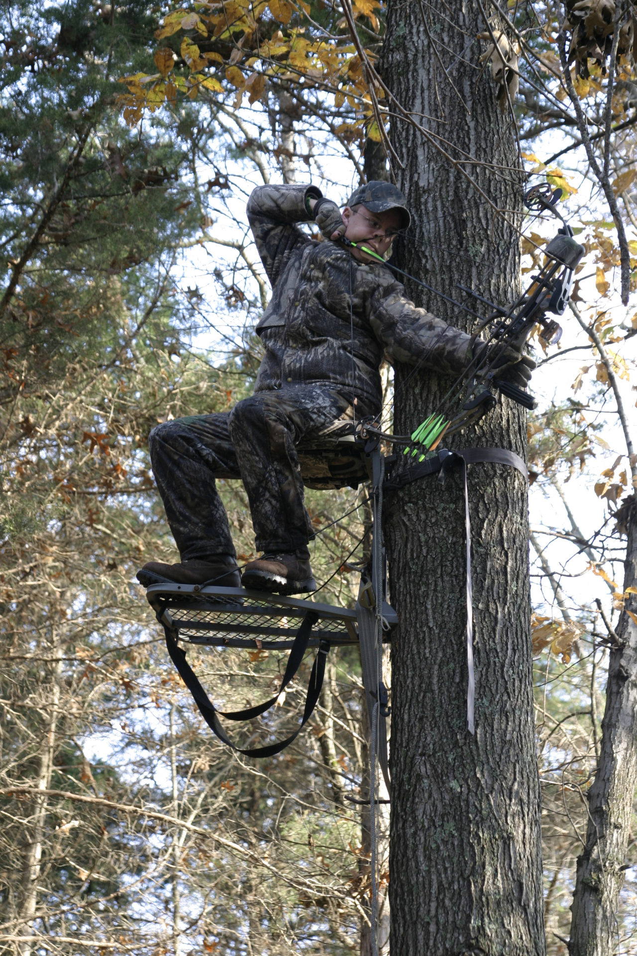 Camouflaged Bowhunter in tree stand at full draw.